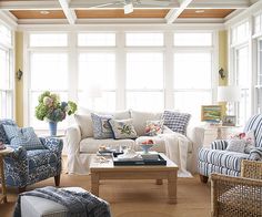 a living room filled with lots of furniture next to two large windows and a ceiling fan