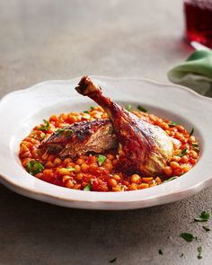 a white bowl filled with beans and meat on top of a table next to a glass of red wine