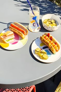 two plates with hotdogs and pickles on them sitting on a table outdoors