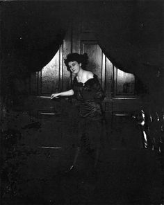 an old photo of a woman standing in front of a door with her arm outstretched