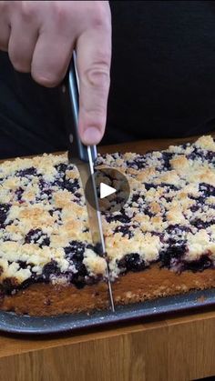 a person cutting into a blueberry cake with a knife