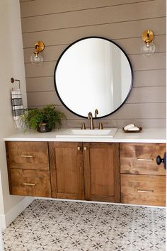 a bathroom vanity with a round mirror above it and wooden cabinets underneath the sink area