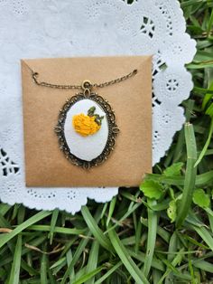 a necklace with an egg on it sitting in the grass next to a piece of paper