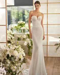 a woman standing in front of flowers wearing a white wedding dress with an open back