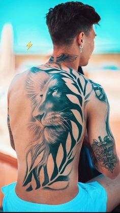 a man with a lion tattoo on his back is sitting in front of the ocean