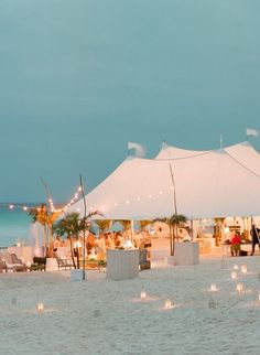 people are sitting under white tents on the beach with candles lit in front of them