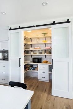 a kitchen with white cabinets and open doors to the pantry area that leads into the dining room