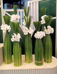 four green vases with white flowers are sitting on a table next to each other