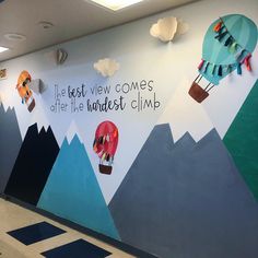 an office wall painted with hot air balloons, mountains and clouds that say it's best view comes after the kindest climb