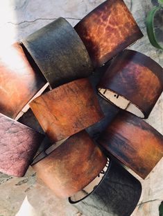 a bunch of brown and black bracelets sitting on top of a stone floor next to a plant