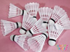 six white plastic badminton racquets on a pink background with black and white pins