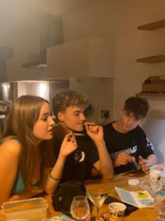 three young people sitting at a table with food and drinks in front of their faces