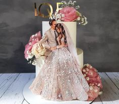 a bride and groom sitting on top of a wedding cake with the word love spelled in gold