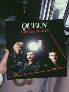 a person holding up a book with the title queen greatest hits on it's cover