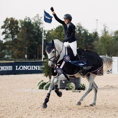 a woman riding on the back of a white horse in a dirt field next to a blue flag