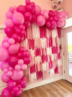 pink and white balloons are hanging on the wall in front of a door with streamers