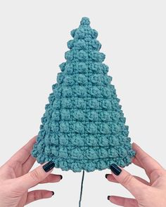 two hands holding up a crocheted blue christmas tree ornament in front of a white background