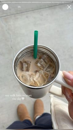 a person holding a cup with ice in it and a green straw sticking out of the top