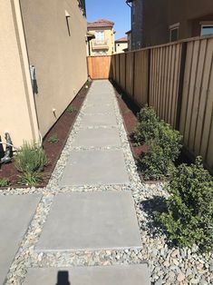 a walkway made out of stones and gravel next to a fence in front of a house