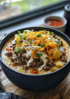 a black bowl filled with soup and cheese on top of a wooden cutting board next to a window