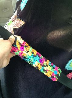 a person is holding a crocheted object in their car seat belt, while wearing a black shirt