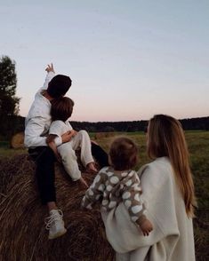 three people sitting on hay bales in the middle of a field with one person reaching up into the sky