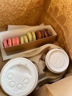 an open box with four macaroons and two coffee cups in it, sitting next to a brown paper bag