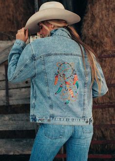 Protect yourself in style with our Dream Catcher Denim Jacket. Featuring a classic trucker style, this high-quality denim jacket is adorned with a colorful embroidered dream catcher, a sacred symbol of protection in Native American cultures. With four functional pockets and roomy interior pockets, this jacket is both fashionable and practical. Hand-embroidered in the USA and available in sizes S-XL. Order yours today and embrace the power of the dream catcher! Allow up to 14 business days Model Bohemian Denim Jacket With Pockets For Fall, Bohemian Denim Jacket With Pockets In Medium Wash, Fall Festival Denim Jacket With Pockets, Bohemian Denim Jacket With Pockets, Casual Denim Jacket With Pockets For Festival, Casual Medium Wash Denim Jacket For Festivals, Bohemian Denim Blue Embroidered Outerwear, Bohemian Embroidered Denim Blue Outerwear, Bohemian Fall Denim Jacket In Medium Wash