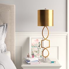 a nightstand with a lamp on it next to a white bed and a framed photograph