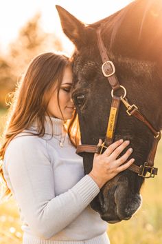 a woman is hugging her horse while standing in the grass with sunlight shining on her face