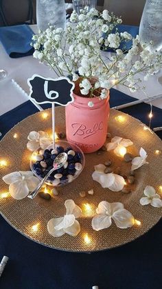 a table topped with a vase filled with white flowers and blueberries on top of a plate