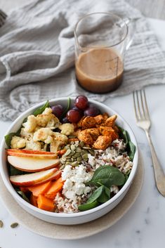 a white bowl filled with rice, fruit and nuts next to a glass of brown liquid