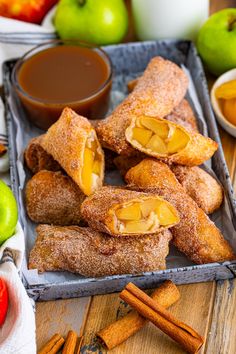 apples and cinnamon rolls are on a tray next to some apple slices, cinnamon sticks, and an apple in a bowl