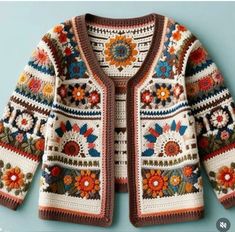 a crocheted cardigan with flowers and leaves on the front, sitting on a blue surface