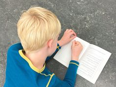 a young boy sitting at a table with a book and pen in his hand while writing on paper