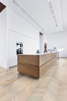 a kitchen with white walls and wood flooring on the side, along with an island