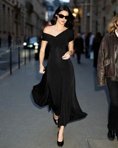 a woman in a black dress walking down the street