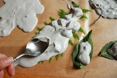 a spoon is being used to decorate fake flowers and leaves on a wooden table with white icing