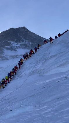 a long line of people climbing up the side of a snow covered mountain