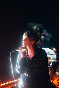 a woman standing in front of a microphone on top of a stage with lights behind her