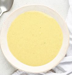 a white bowl filled with soup next to two spoons on top of a table