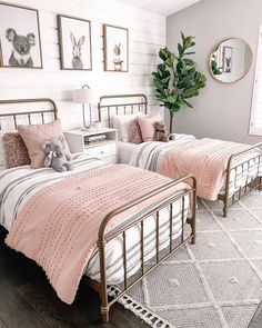 two beds in a bedroom with pink comforters and pictures on the wall above them