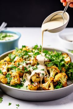 someone pouring dressing onto a plate of roasted cauliflower