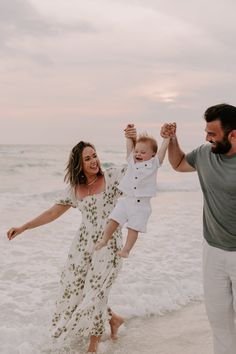 a man and woman are holding their child up in the air while walking on the beach