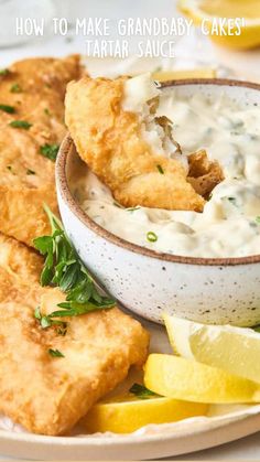 a white plate topped with fried fish and lemon wedges next to a bowl of sour cream sauce