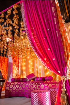 a bed covered in pink and orange sheets next to a wall with lights on it