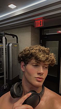 a shirtless man with headphones standing in front of a gym equipment machine and looking at the camera