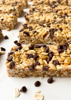 chocolate chip granola bars cut into squares on top of a white surface with oats scattered around them