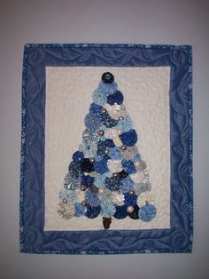 a blue and white quilted christmas tree with ornaments in it's center, hanging on the wall