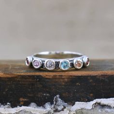 a ring with five different colored stones on top of a piece of drift wood in front of a wall